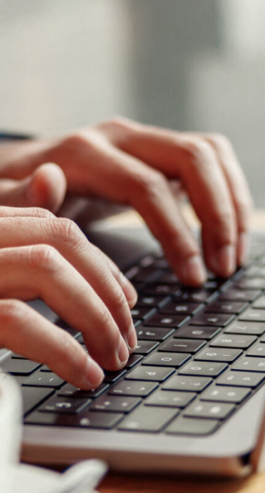 Nahaufnahme eines Geschäftsmannes, der im Café an einem Laptop arbeitet. Im Vordergrund eine Kaffeetasse auf einem Holztisch